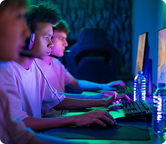 Grupa graczy e-sportowych grających na komputerach gamingowych, noszących zestawy słuchawkowe i w pełni skoncentrowanych podczas emocjonującego meczu wieloosobowego w otoczeniu rozświetlonym neonami.