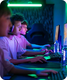 Grupa graczy e-sportowych grających na komputerach gamingowych, noszących zestawy słuchawkowe i w pełni skoncentrowanych podczas emocjonującego meczu wieloosobowego w otoczeniu rozświetlonym neonami.